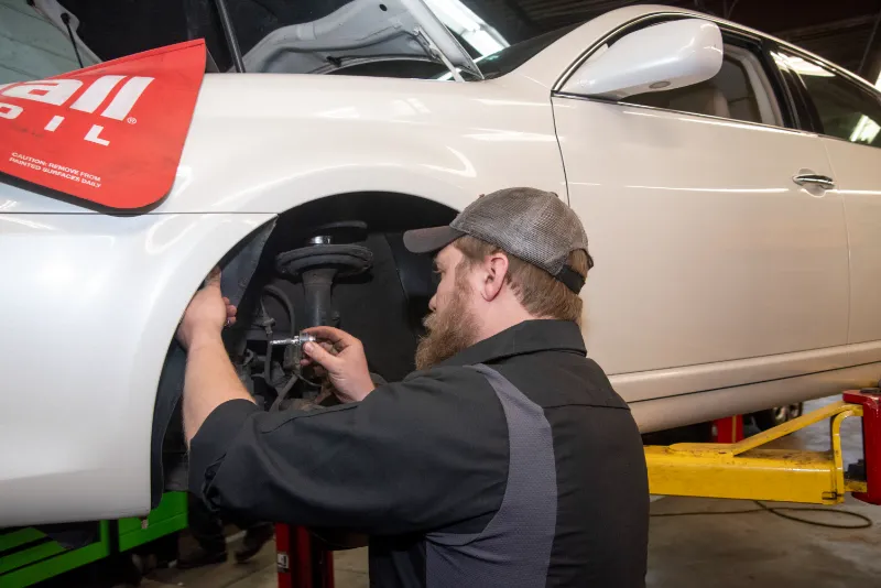 Auto technician works on front wheel area with car elevated on lift in Doylestown, PA