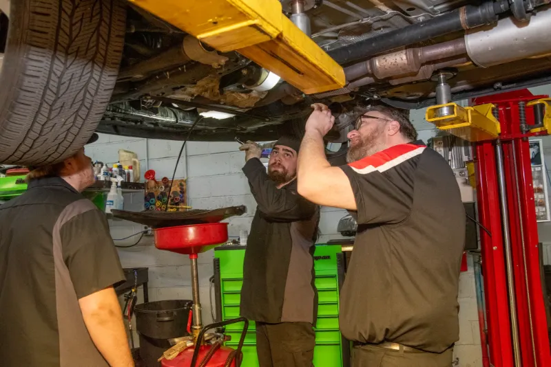 Three Doylestown, PA technicians inspecting the underside of a lifted vehicle in a garage