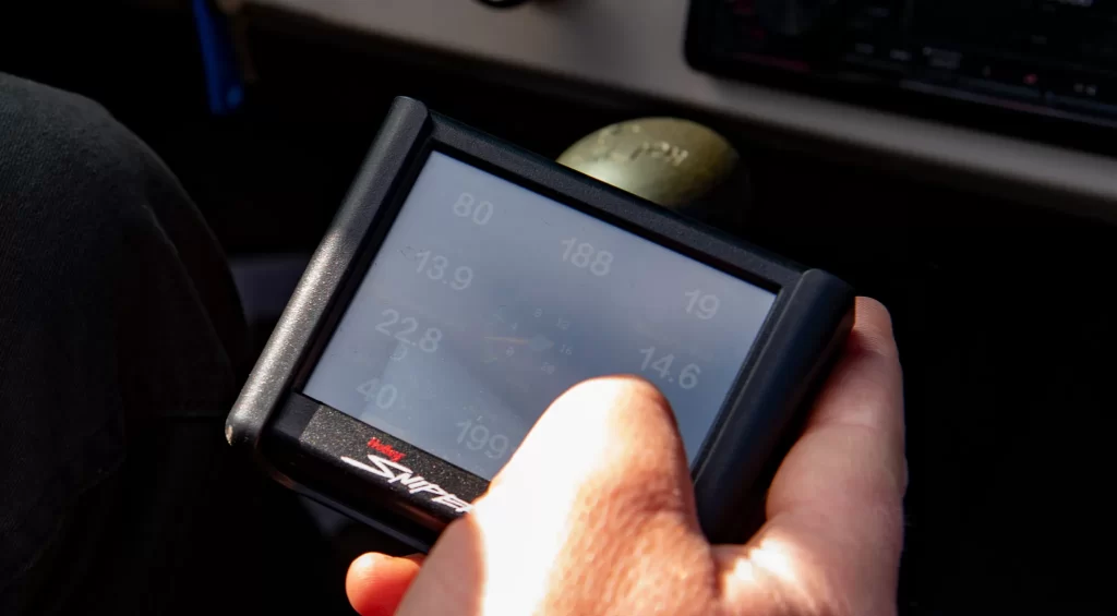 Hand operates electronic engine tuning interface near gear shifter in car interior