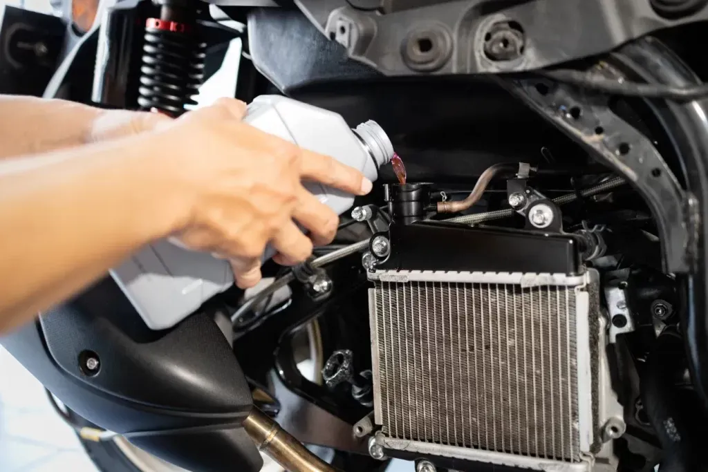 Close-up of hands pouring coolant from a plastic bottle into a motorcycle or small engine radiator in Doylestown. PA