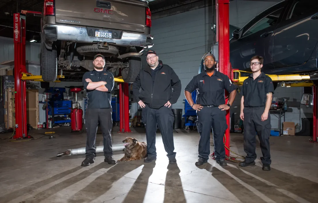 Four mechanics and a dog in Doylestown, PA pose in a garage with cars on lifts