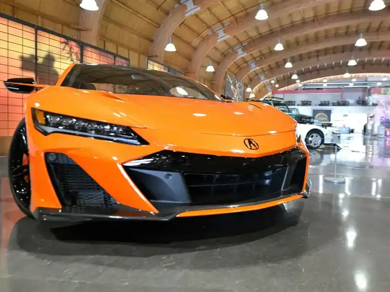 Low-angle front view of an orange Acura sports car in an indoor showroom