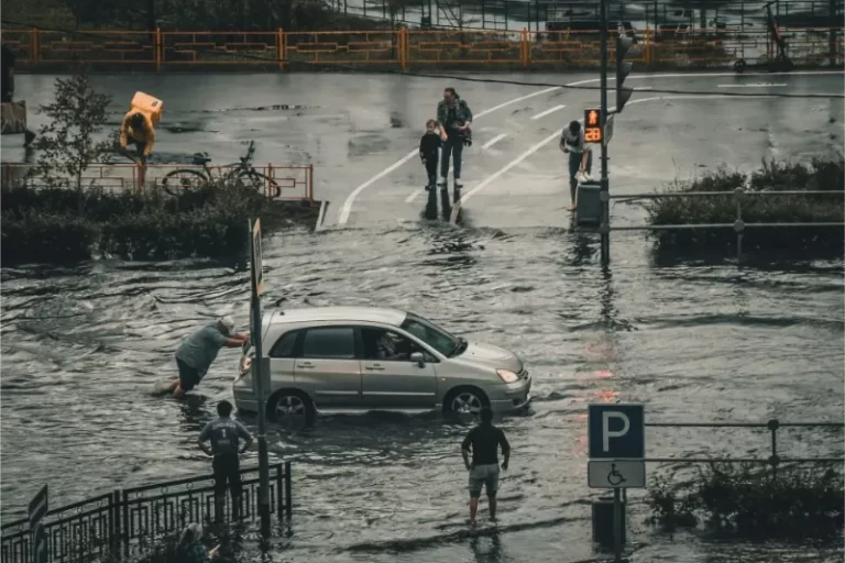 People help push a stranded car through deep floodwater on a city street