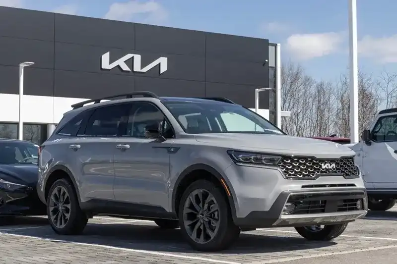 Silver Kia SUV parked in front of a dealership with Kia signage visible