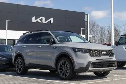 Silver Kia SUV parked in front of a dealership with Kia signage visible
