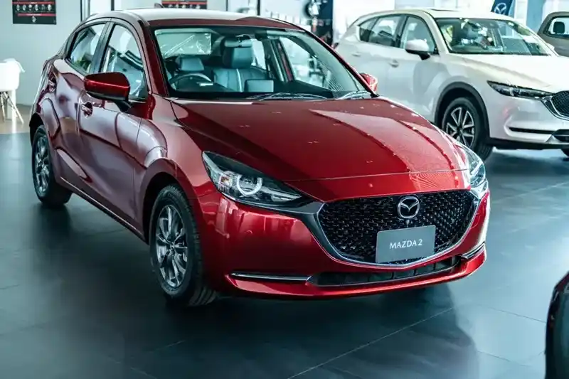 New red Mazda compact car shown under showroom lighting with a visible nameplate